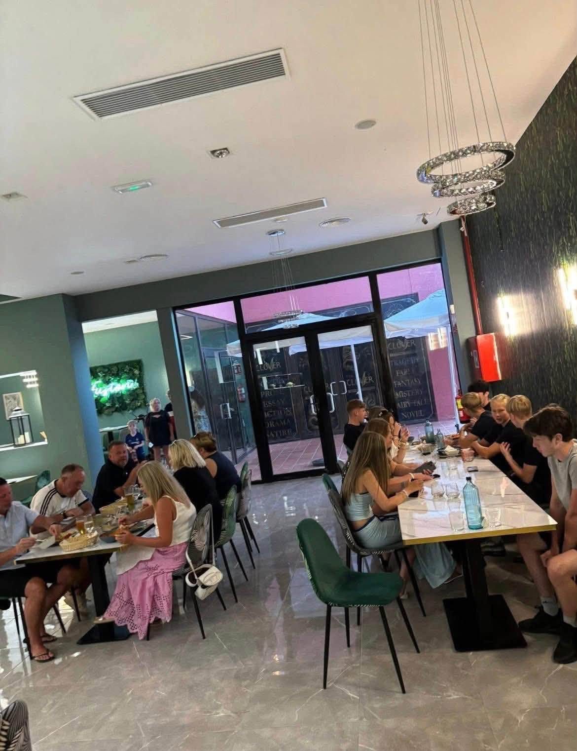 Guests dining among sage green walls, botanical chairs and the neon Fusión sign