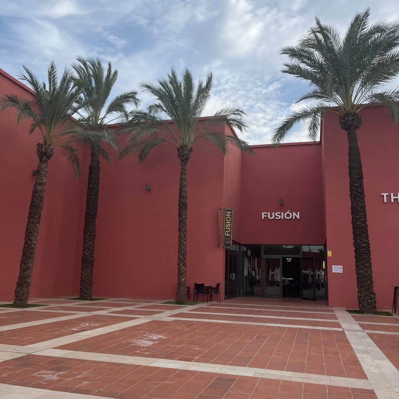 The terracotta-red entrance of Fusión framed by tall palm trees